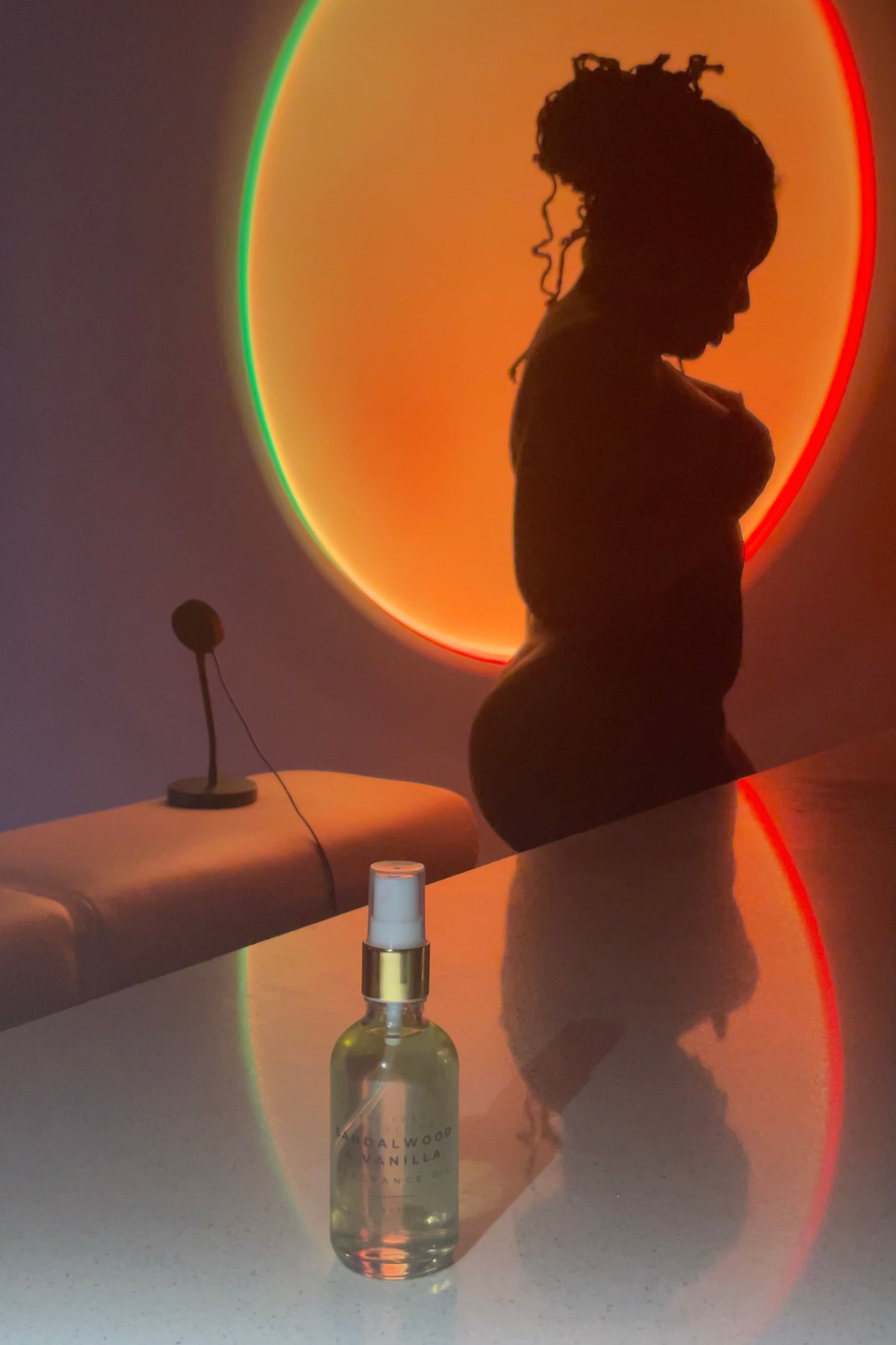 Silhouette of a person against a colorful circular light, with a bottle of perfume in the foreground.
