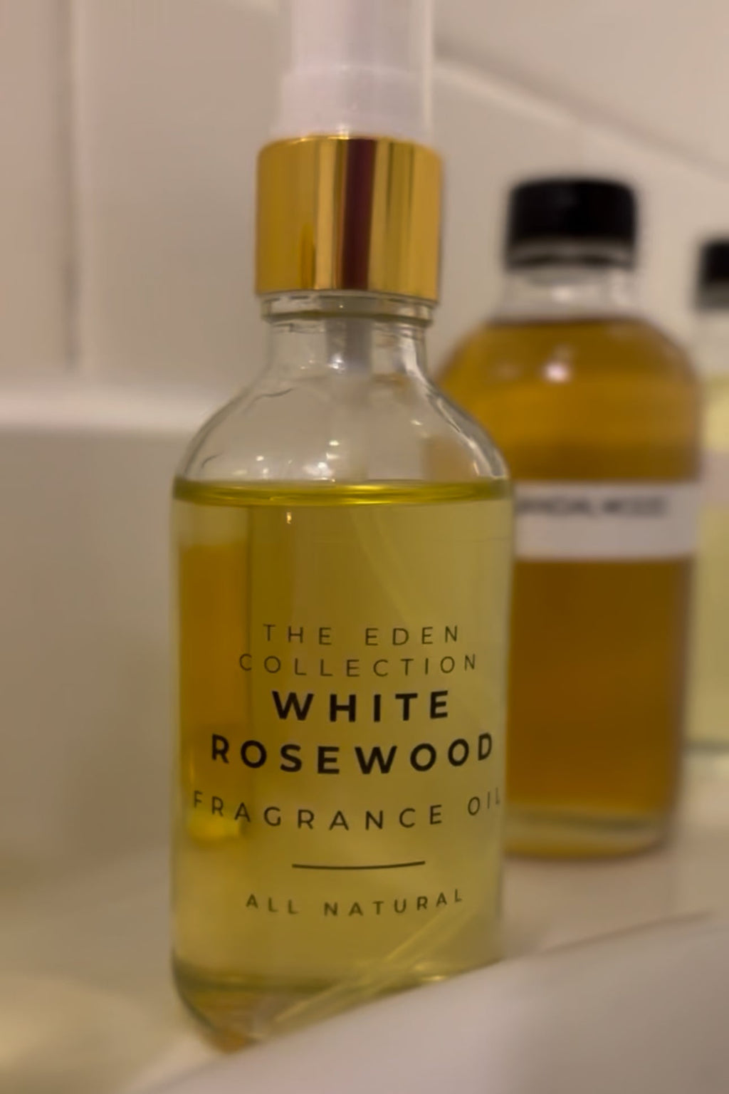 White Rosewood fragrance oil bottle with gold cap on a blurred background