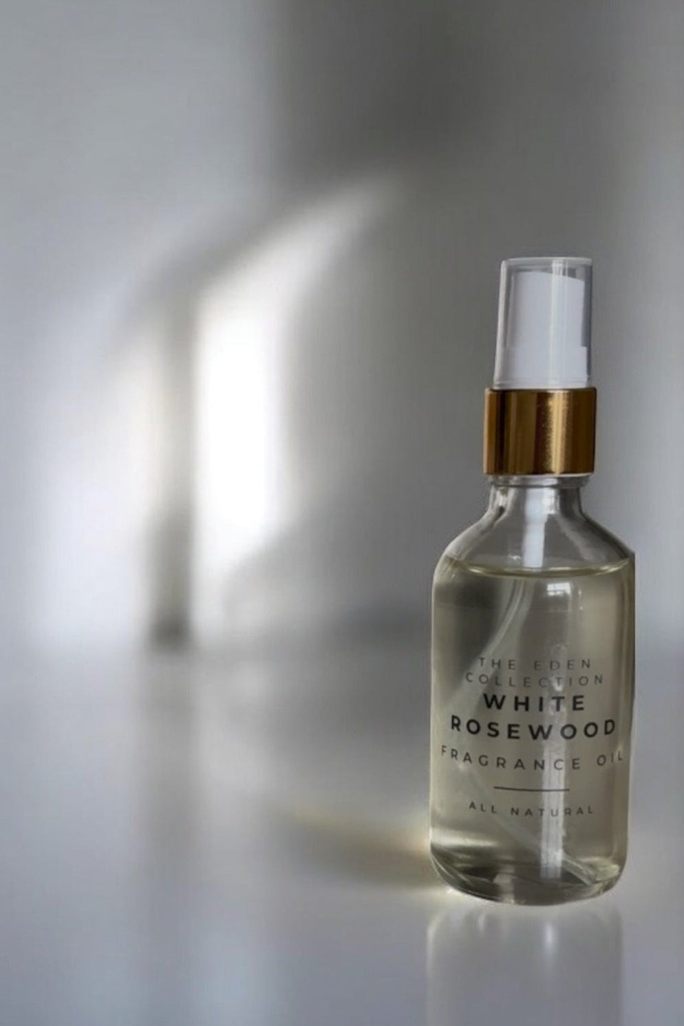 Clear glass bottle with gold cap labeled 'White Rosewood' on a reflective surface.
